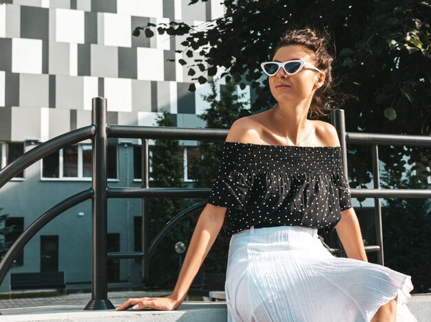 Beautiful smiling model dressed in elegant summer clothes.Sexy carefree girl sitting in the street.Trendy modern businesswoman in sunglasses having fun