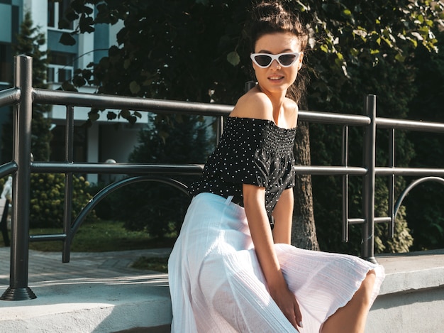 Beautiful smiling model dressed in elegant summer clothes.Sexy carefree girl sitting in the street.Trendy modern businesswoman in sunglasses having fun