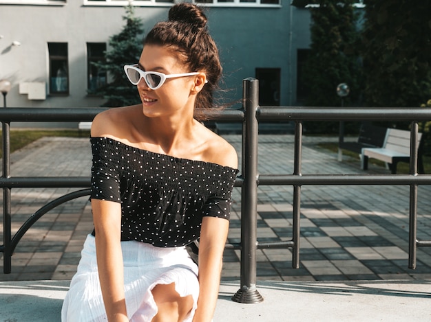 Beautiful smiling model dressed in elegant summer clothes.Sexy carefree girl sitting in the street.Trendy modern businesswoman in sunglasses having fun