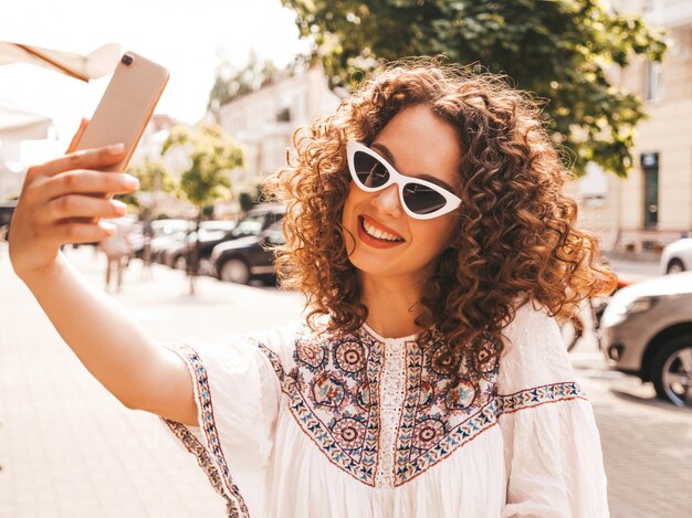 Beautiful smiling model with afro curls hairstyle dressed in summer hipster white dress.