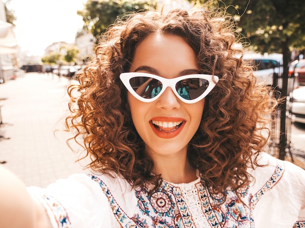 Beautiful smiling model with afro curls hairstyle dressed in summer hipster white dress.