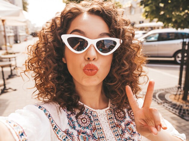 Beautiful smiling model with afro curls hairstyle dressed in summer hipster white dress.