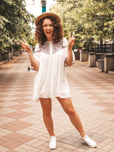 Beautiful smiling model with afro curls hairstyle dressed in summer hipster white dress.