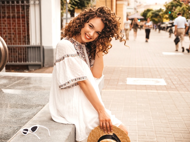 Beautiful smiling model with afro curls hairstyle dressed in summer hipster white dress.