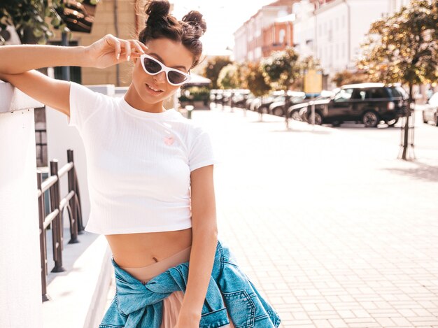 Beautiful smiling model with horns hairstyle dressed in summer hipster jacket jeans clothes.Sexy carefree girl posing in the street.Trendy funny and positive woman having fun in sunglasses