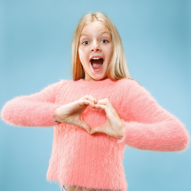 Free photo beautiful smiling teen girl makes the shape of a heart with her hands on the blue wall