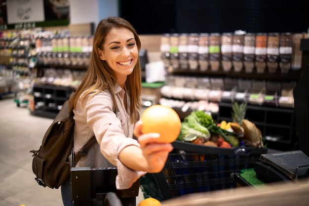 Beautiful smiling woman buying oranges in supermarket at fruit department