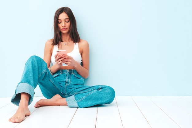 Beautiful smiling woman dressed in white jersey top shirt and jeans. carefree cheerful model using her smartphone