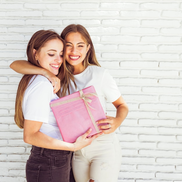 Beautiful smiling women with birthday gift in front of brick wall