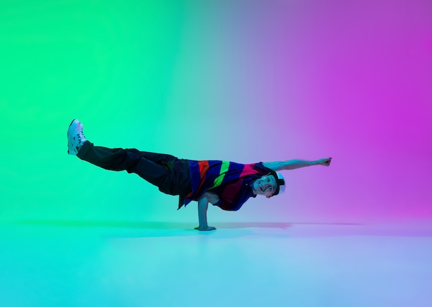 Free photo beautiful sportive boy dancing hip-hop in stylish clothes on colorful gradient wall at dance hall in neon light. youth culture, movement, style and fashion, action. fashionable bright portrait.