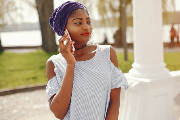 A beautiful and stylish dark-skinned girl walks in a sunny summer city