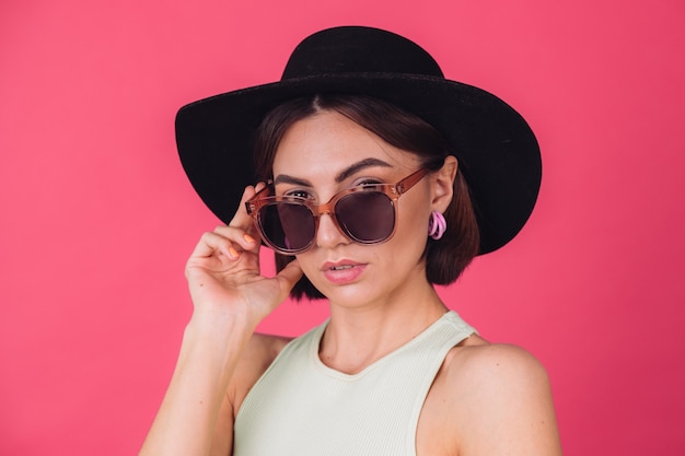 Free photo beautiful stylish woman in hat and sunglasses posing over pink red wall