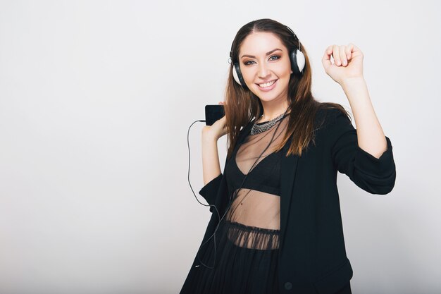 Beautiful stylish woman isolated in black suit listening to music on headphones dancing