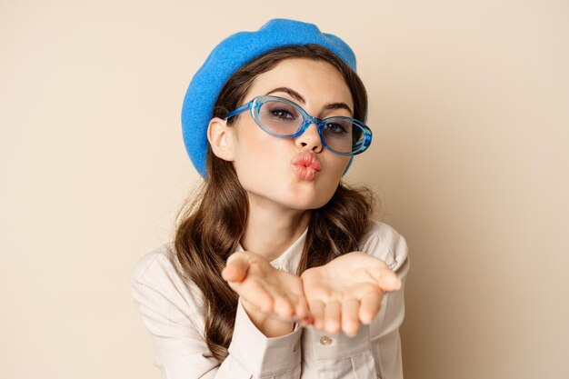 Beautiful stylish woman in sunglasses blowing air kiss on hands near lips gazing softly and flirty a...