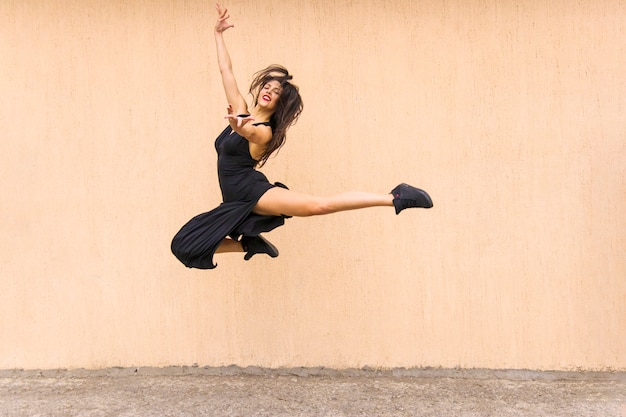 Beautiful tango dancer jumping in air against wall backdrop