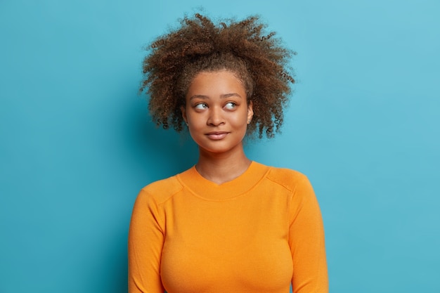 Free photo beautiful thoughtful afro american woman with curly hair healthy dark skin looks aside thinks deeply wears casual jumper.