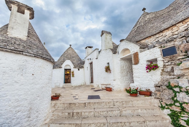 Beautiful town of Alberobello with Trulli houses among green plants and flowers, main touristic district, Apulia region, Southern Italy. Typical whitewashed buildings built with a dry stone walls and