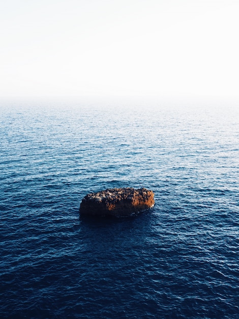 Beautiful vertical shot of a brown rock in the middle of the sea with amazing water textures