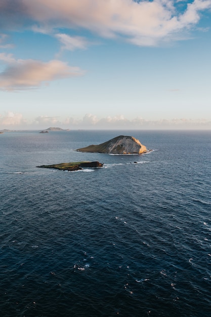 Free photo beautiful vertical shot of small hills in the sea under the cloudy sky during daytime