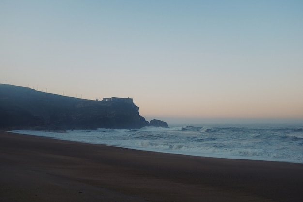 Free photo beautiful view of a big rock with a castle on top and big waves alert sunset