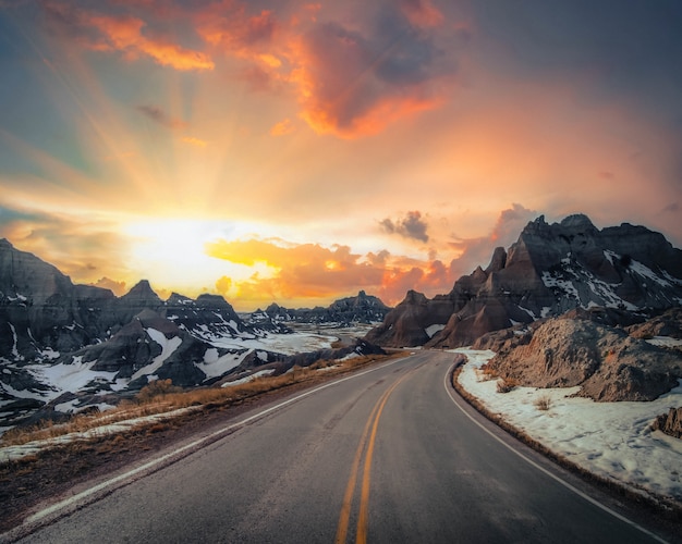 Beautiful vista of a narrow countryside road with rocky mountains covered in snow in the distance