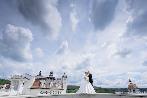 Free photo beautiful wedding couple is standing near the church with beautiful cloudy sky