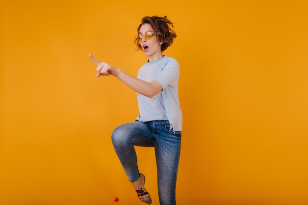 Beautiful white woman in trendy denim pants jumping on yellow space