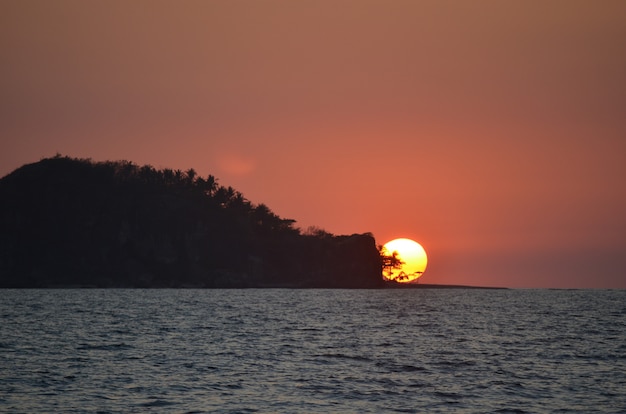 Free Photo beautiful wide silhouette shot of an islet covered with trees on by the sea under sky during sunset