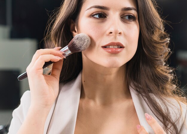 Beautiful woman applying makeup by brush 