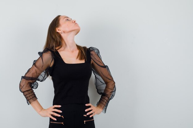 Free Photo beautiful woman in black blouse looking away while holding hands on her waist and looking offended 