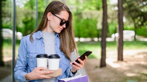 Free photo beautiful woman carrying coffee while checking phone