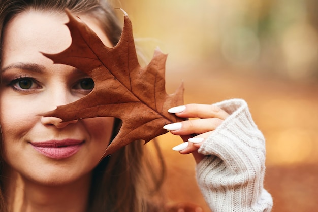 Free photo beautiful woman covering her face with autumn leaves