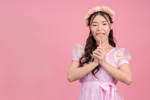 A beautiful woman dressed in a pink princess is playing with her sweet candy on a pink .