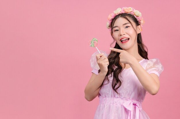 A beautiful woman dressed in a pink princess is playing with her sweet candy on a pink .