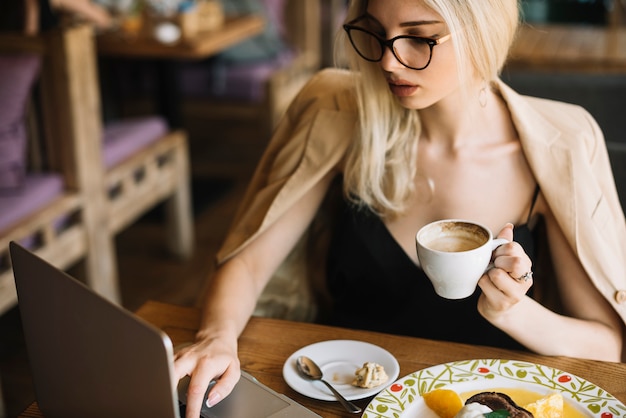 Free photo beautiful woman drinking coffee in the caf��� while using laptop