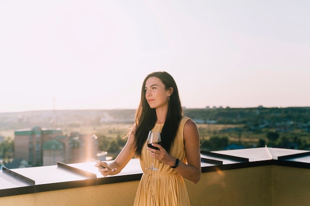 Free photo beautiful woman drinking wine on the rooftop in the sunlight