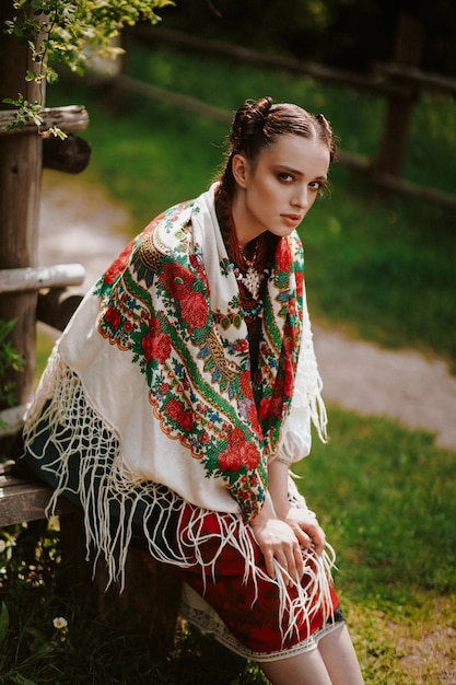 Free Photo beautiful woman in an embroidered traditional dress is sitting on the bench and looking