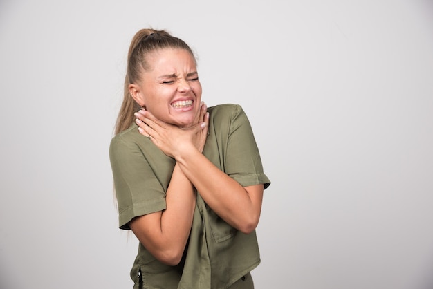 Beautiful woman having neckache on gray wall.