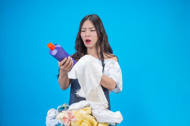 A beautiful woman holding a cloth and liquid detergent prepared for washing on blue