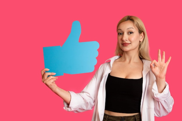 Free photo beautiful woman holding a like button isolated on pink background