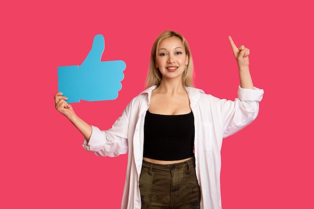 Beautiful woman holding a like button isolated on pink background