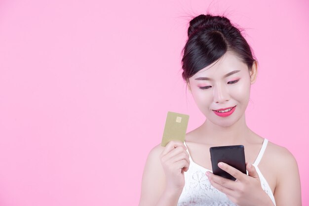 Beautiful woman holding a smartphone and card on a pink background