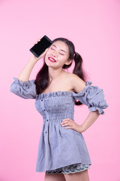 Beautiful woman holding a smartphone on a pink background.