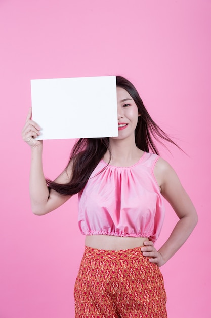 Beautiful woman holding a white board sheet on a pink background.