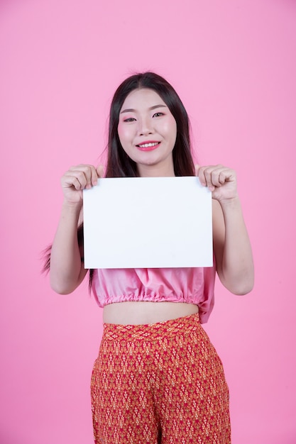 Free Photo beautiful woman holding a white board sheet on a pink background.