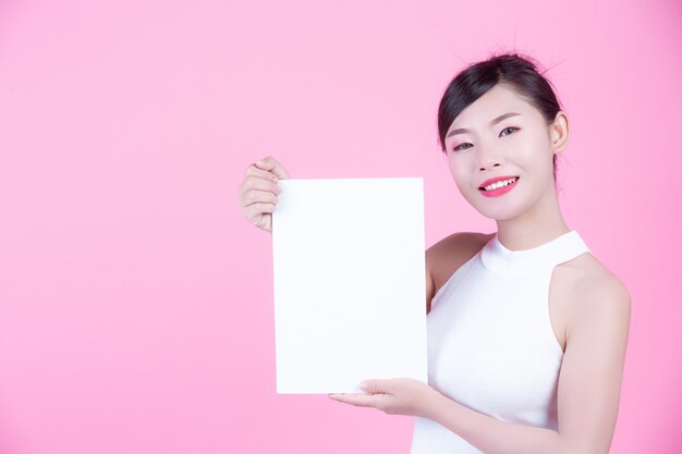 Beautiful woman holding a white board sheet on a pink background.