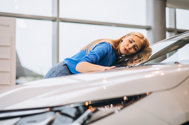 Beautiful woman hugging a car in a car showrrom