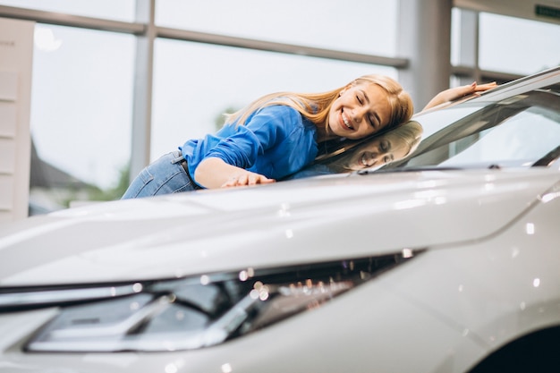 Beautiful woman hugging a car in a car showrrom