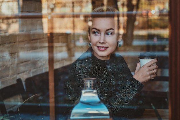 Free photo beautiful woman is enjoying her coffee while sitting at cafe near window.