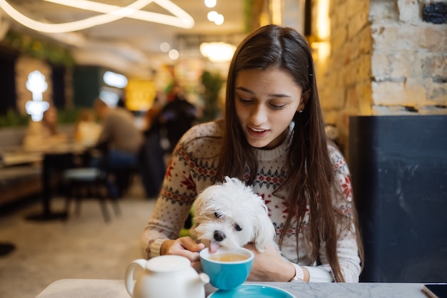 Free Photo beautiful woman is holding her cute dog, drinking coffee and smiling in cafe